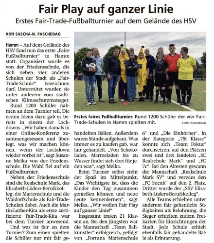 Auf dem Bild ist ein Artikel zu sehen, der über das Fair-Trade-Fußballturnier der Hammer Fair-Trade-Schulen berichtet. Das Foto zeigt die Schulleitung, das Fairtrade-Team und weitere Beteiligte des Turniers auf dem Fußballfeld.